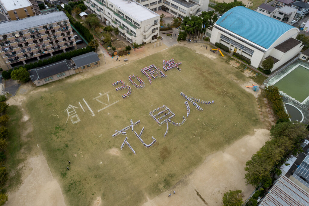角度を変えた花見小学校のグラウンドに整列した人文字のドローン撮影